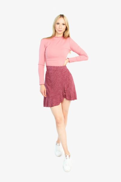 Das Model trägt einen Wickelrock in bordeaux mit rosé farbenen Pünktchen. Durch die Volants wirkt der Minirock verspielt.